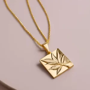 Pendentif de løv en or composé d'une chaine et d'un carré sculptée d'une feuille par l'artiste Méta.